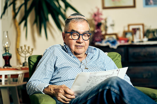Jewish senior with glasses sitting in the armchair reading a torah book