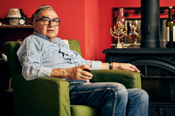 Pensive Jewish senior sitting in the armchair and drinking kosher wine