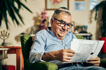 Jewish senior with glasses sitting in the armchair reading a torah book