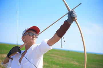 teenager boy trains to shoot from a classic wooden bow in the field