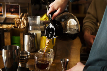man's hand pouring coffee into cup glass