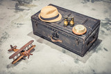 Vintage old classic travel trunk luggage with leather handles circa early 1900s, wooden toy plane, compass, binoculars, men's hat. Travel by air concept. Retro style filtered photo