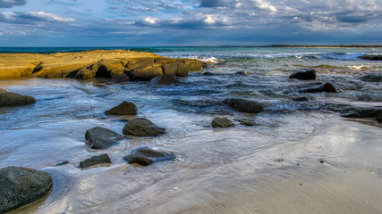 Large rocks and boulders in calm shallow sea water soft waves blue sky with clouds, wide image 