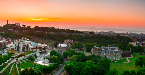 View over the Palace of Holyroodhouse, Scottish Parliament and Calton Hill under orange sunset sky in Edinburgh, Scotland