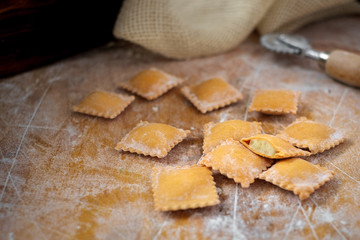 Uncooked rustic style ravioli orange color on a kitchen wooden table