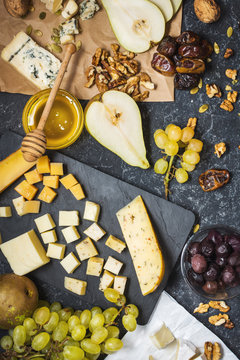 Different types of cheese on board, olive, fruits, almond and wine glasses on black stone table