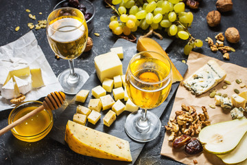 Different types of cheese on board, olive, fruits, almond and wine glasses on stone table