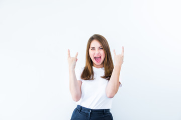 Fototapeta na wymiar Happy excited young woman showing the sign of rock and roll sigh isolated on white background. Emotional girl flirting at camera and showing dancing gesture.Positive emotion expression. Copy space.