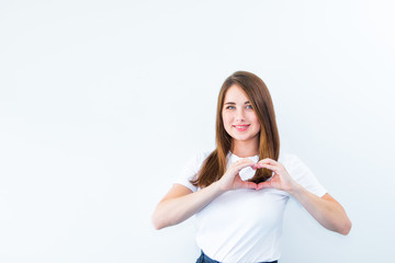 Portrait of young, brunette, pretty girl in white T shirt showing with her finger heart shape, sending love. Cancer protect. Isolated on white background. Human emotions. Selective focus, copy space.
