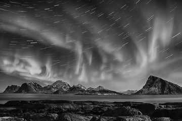 Northern Lights, Aurora Borealis shining in night starry sky with star tracks at winter Lofoten...
