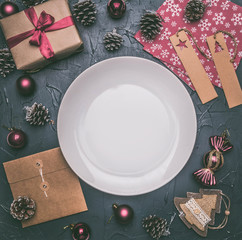 Christmas concept, postcard, gift box, Christmas toys and cones, on a grey background, lined around a white plate