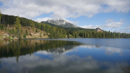 Fototapeta na wymiar Strbske pleso and Tatra peaks visible from the back. A village located in the valley, from which tourists are moving to the Tatras. Colorful waters of a mountain pond, blue sky and unending peaks.