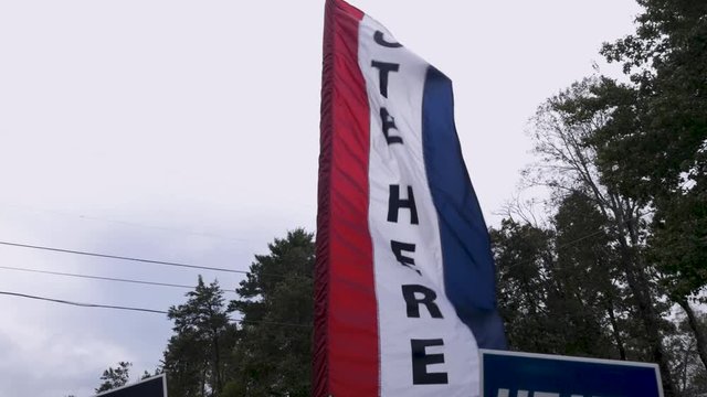 Slow motion of a red white and blue vote here sign blowing in the wind