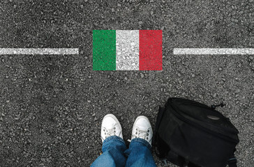  a man with a shoes and backpack is standing on asphalt next to flag of italy and border