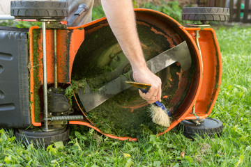 Man's hand with brush cleaning lawn mower