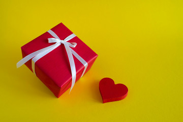 Red gift box with red heart on yellow background. Copy space.