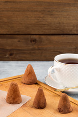 Chocolate candies in the shape of a cone on a wooden background, white mug with tea.