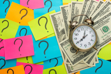 alarm clock on the background of question marks and US dollars, the concept of earning money, ideas for salary, and loss of time and money