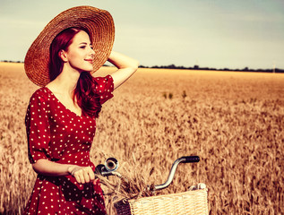 Redhead girl with bicycle on wheat field.