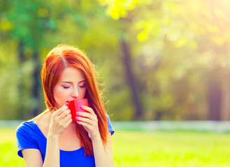 Redhead girl with orange cup at green lawn in summertime