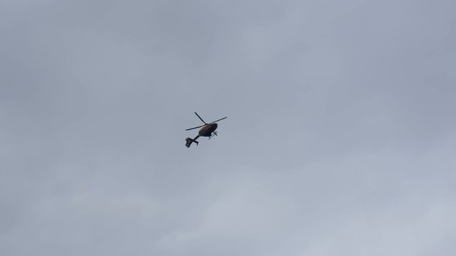 Helicopter marked Police is flying in overcast sky above in England, United Kingdom