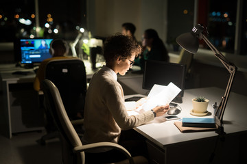 Side view portrait of young businesswoman working late in dark office, copy space