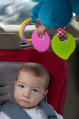 Fototapeta na wymiar Baby boy sitting in child car seat with rattle hanging from ceiling