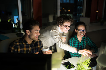 Group of three smiling young people working together in dark office late at night, copy space