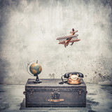 Vintage old classic travel trunk luggage with leather handles circa early 1900s, flying wooden toy plane, rotary telephone and aged globe. Travel by air concept. Retro style filtered photo
