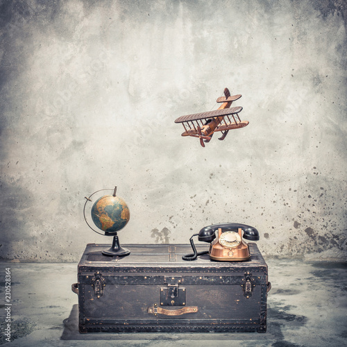 Vintage old classic travel trunk luggage with leather handles circa early 1900s, flying wooden toy plane, rotary telephone and aged globe. Travel by air concept. Retro style filtered photo