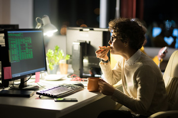 Side view portrait of young woman eating snacks at workplace while working in office at night