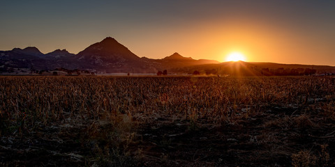 Sunset over harvested field with sunbeams and mountains