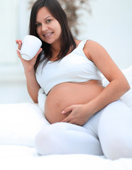 happy pregnant woman drinking milk sitting in the living room.