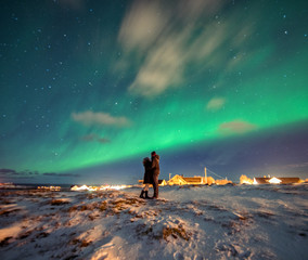 A couple admires the Northern Lights in the mountains of Reine, Norway.  Lofoten Islands - obrazy, fototapety, plakaty