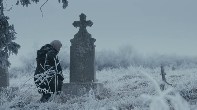 Woman praying in front of an old tombstone