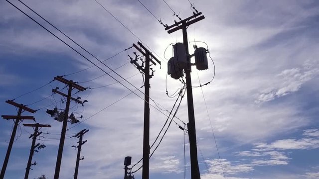 A slow tracking dolly shot looking up at a telephone or utility pole with the sunlight glowing behind.  	