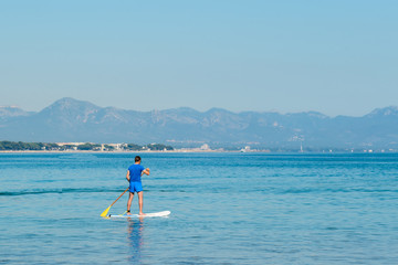 Fototapeta na wymiar Stand up paddle boarding. Young man floating on SUP board