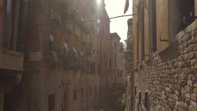 Wide tilt up shot of historic water canal street Cale Castagna with brick wall, sun flares lens, Venice, Italy