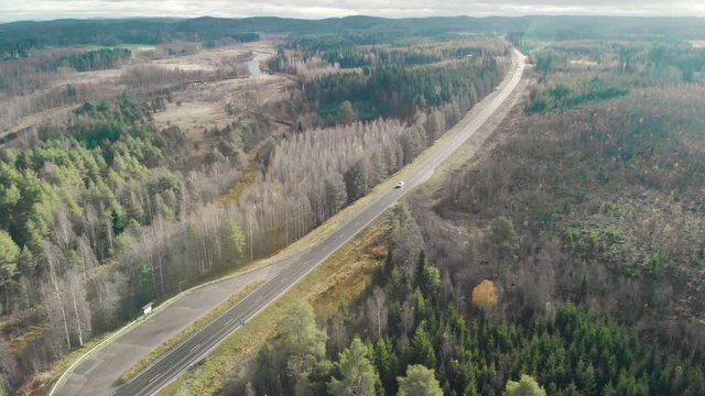 Aerial, tilt down, drone shot, flying towards cars on a road and leafless autumn forest, on a sunny fall day, in Juuka, Pohjois-Karjala, Finland