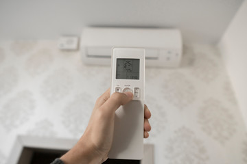 Hand with remote control directed on the conditioner on the wall. Man's hand using remote control open The air conditioner is cooled to 25 degrees Celsius in his bedroom.