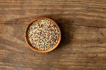 Bowl of organic red, black and yellow quinoa on wooden farm kitchen table.