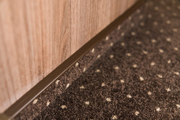 Brown carpet floor with a white dots with a carpet baseboard on a wood-based panels wall.