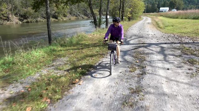 Pretty, mature woman on a mountain bike riding on a gravel road with a river on one side and farmland on the other.