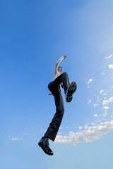 青空をバックにジャンプするYシャツ姿の若いビジネスマン1人。元気・パワー・成功・挑戦イメージ