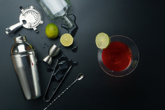 Cosmopolitan cocktail and bar equipments, stainless steel cocktail shaker and jigger, bar spoon with strainer, empty vodka bottle, the lemons and ice tongs with ice cubes on the table