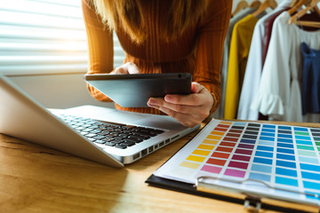 Fashion designer woman talking smart phone and using laptop with digital tablet computer in modern studio in morning light