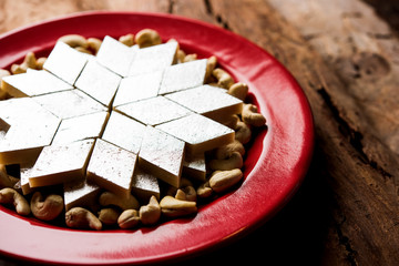 Kaju Katli is a Diamond shape Indian sweet made using cashew sugar and mava, served in a plate or bowl over moody background. selective focus