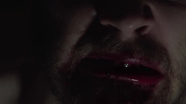 Creepy man zombie, cannibal furiously eating raw meat with frenzy. Blood drips from the mouth. Horror, halloween concept