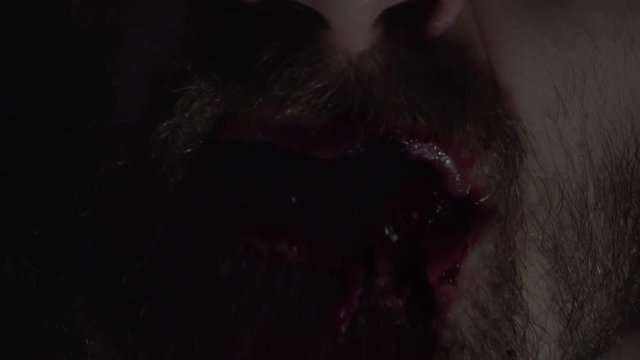 Creepy man zombie, cannibal furiously eating raw meat with frenzy. Blood drips from the mouth. Horror, halloween concept