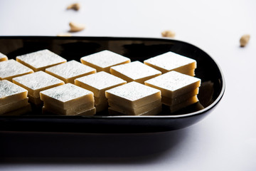 Kaju Katli is a Diamond shape Indian sweet made using cashew sugar and mava, served in a plate or bowl over moody background. selective focus